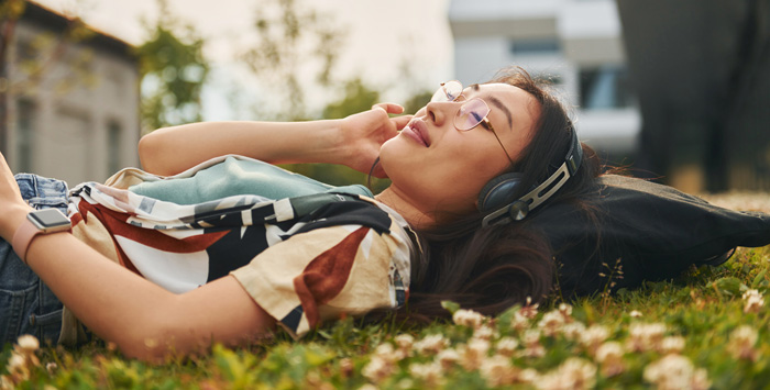 Woman relaxing outdoors, listening to binaural beats to increase her theta wave activity. Woman relaxing outdoors, listening to binaural beats to increase her theta wave activity.