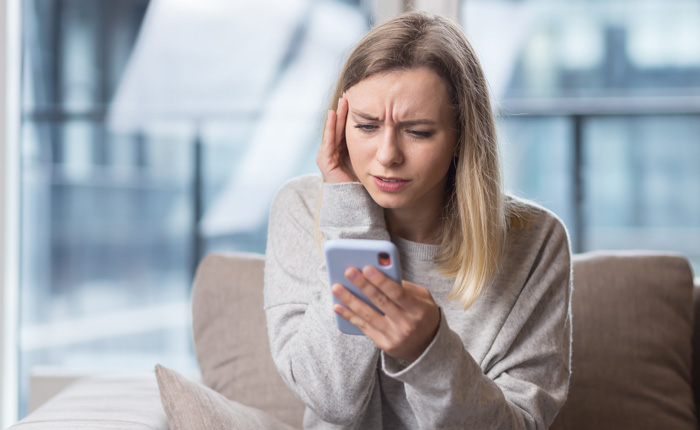 Young woman anxious and fearful viewing iPhone. Social media comparison and mental health have become a dangerous issue. Young woman anxious and fearful viewing iPhone. Social media comparison and mental health have become a dangerous issue.