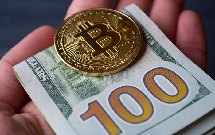 Gold Bitcoin and $100 dollar bill in hand. Gold Bitcoin and $100 dollar bill in hand.