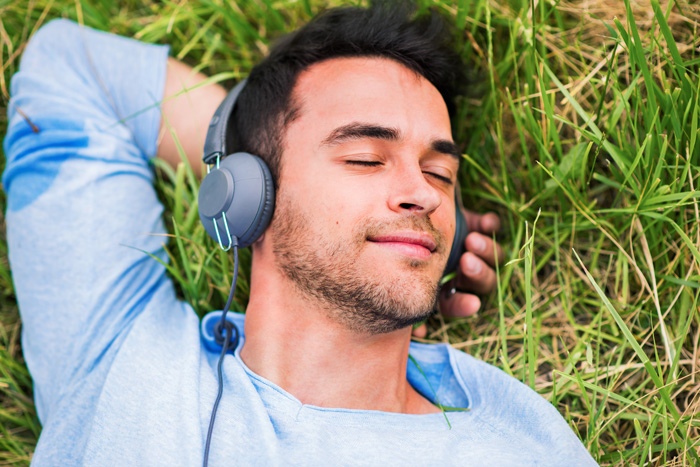 Man relaxing on grass listening to binaural beats to increase Theta brain wave activity and enhance his mental health. Man relaxing on grass listening to binaural beats to increase Theta brain wave activity and enhance his mental health.