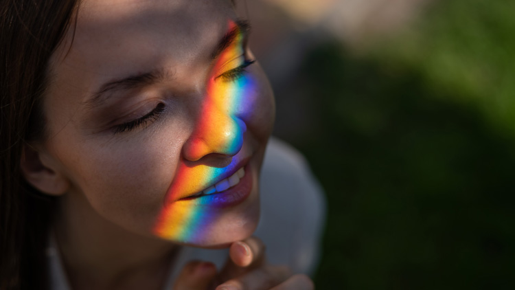 Young woman enjoying the peaceful vibes of a sunlight rainbow from a crystal suncatcher. Young woman enjoying the peaceful vibes of a sunlight rainbow from a crystal suncatcher.