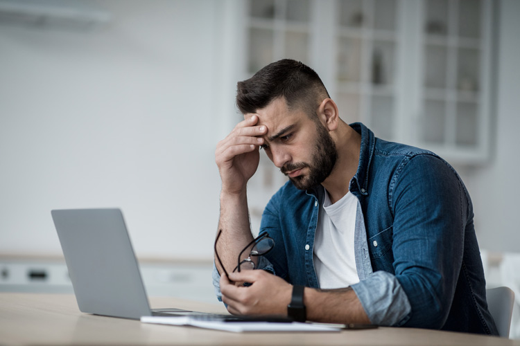 Young guy feeling drained of all joy while viewing his laptop.