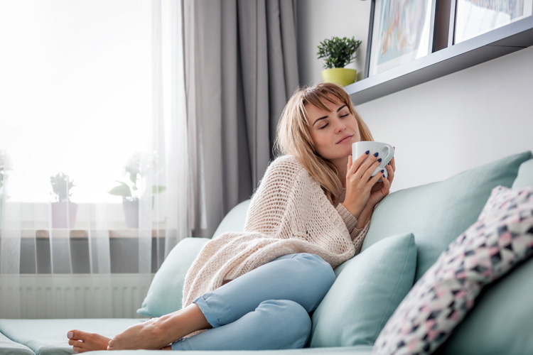 Woman on couch with hot tea and a soft throw blanket to relieve stress. Woman on couch with hot tea and a soft throw blanket to relieve stress.