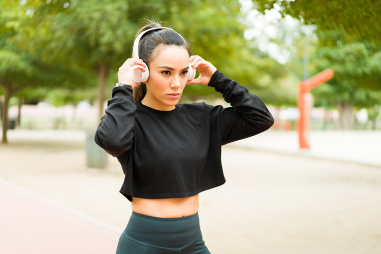 Young lady putting on headphones at the park to begin working out. Young lady putting on headphones at the park to begin working out.