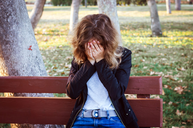 Young woman on park bench drained of her joy because she will not forgive herself.