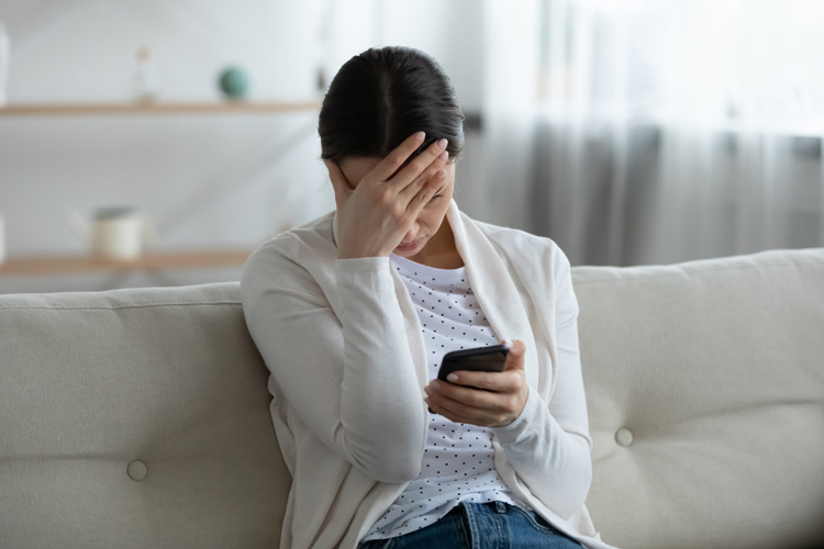 Young woman with phone feeling drained of joy on her couch.